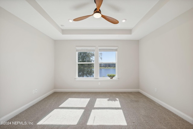 empty room featuring a tray ceiling, light carpet, a water view, and ceiling fan