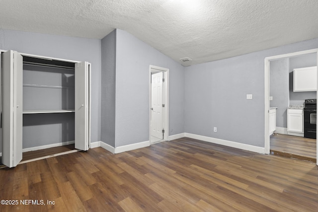 unfurnished bedroom with a textured ceiling, dark wood-type flooring, connected bathroom, a closet, and vaulted ceiling
