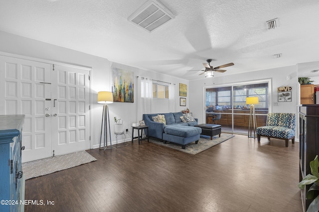 living room featuring dark wood-type flooring, a wealth of natural light, ceiling fan, and a textured ceiling