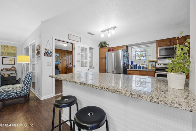 kitchen featuring dark wood-type flooring, light stone counters, a textured ceiling, a breakfast bar area, and appliances with stainless steel finishes