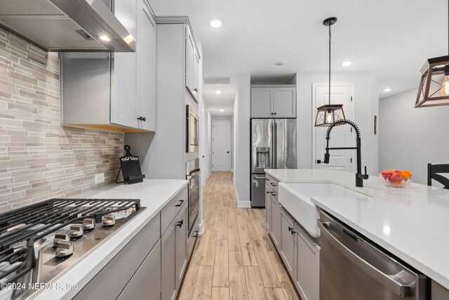 kitchen with gray cabinetry, wall chimney range hood, stainless steel appliances, and light hardwood / wood-style flooring