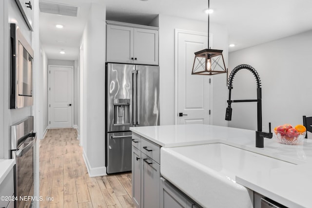 kitchen featuring gray cabinetry, sink, light wood-type flooring, appliances with stainless steel finishes, and decorative light fixtures