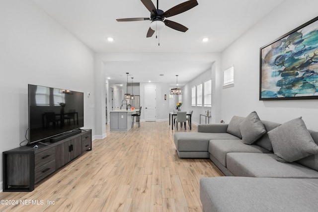 living room with ceiling fan with notable chandelier, light hardwood / wood-style flooring, and sink