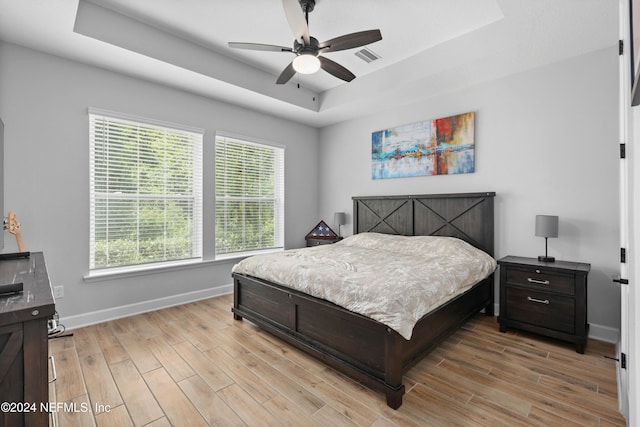 bedroom with ceiling fan, a raised ceiling, and light hardwood / wood-style flooring