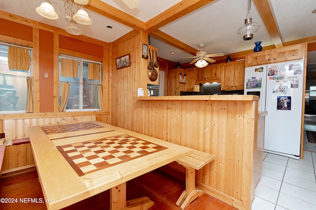 kitchen featuring wood walls, light tile patterned flooring, white fridge, and pendant lighting