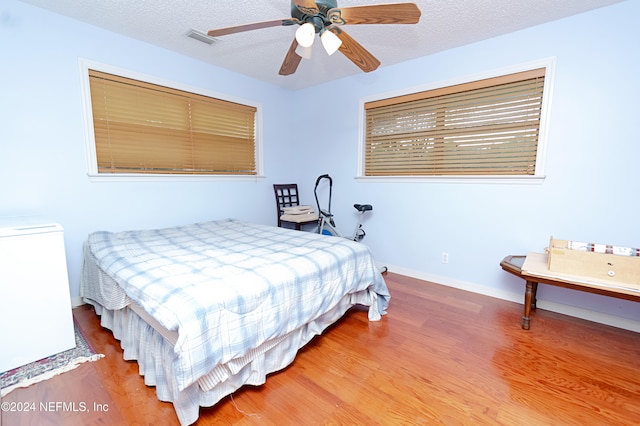 bedroom with hardwood / wood-style flooring, ceiling fan, and a textured ceiling