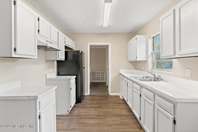 kitchen featuring black refrigerator, a textured ceiling, hardwood / wood-style flooring, sink, and white cabinetry