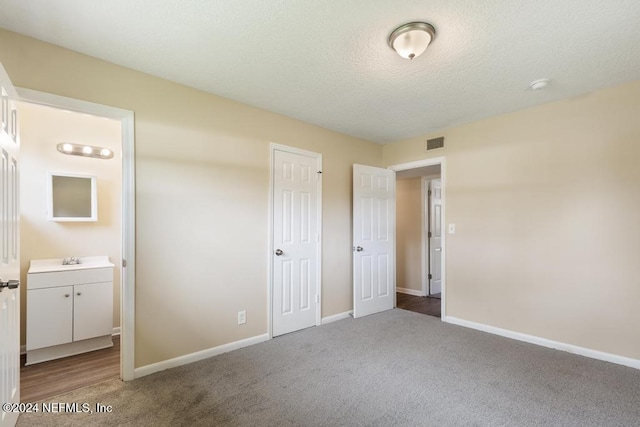 unfurnished bedroom featuring sink, carpet, a textured ceiling, and ensuite bathroom