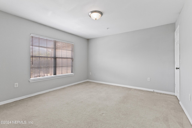 spare room featuring light colored carpet and baseboards