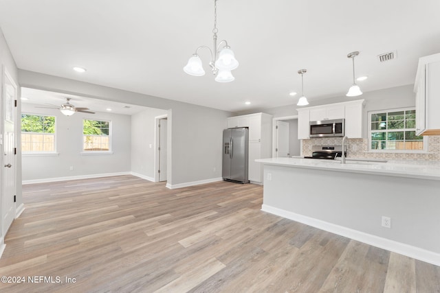 kitchen with light hardwood / wood-style floors, white cabinetry, appliances with stainless steel finishes, hanging light fixtures, and decorative backsplash