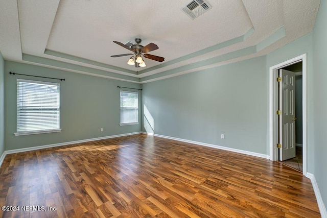 unfurnished room with ceiling fan, dark hardwood / wood-style flooring, a tray ceiling, and a textured ceiling