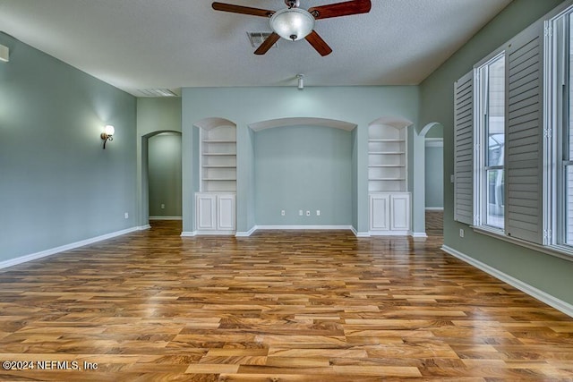 unfurnished living room with a textured ceiling, ceiling fan, hardwood / wood-style floors, and built in shelves