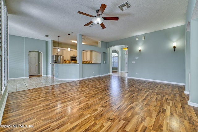 unfurnished living room with ceiling fan, light hardwood / wood-style floors, and a textured ceiling