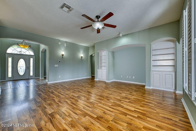 unfurnished living room featuring a textured ceiling, ceiling fan, built in features, and wood-type flooring