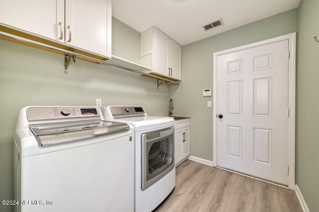 washroom with light hardwood / wood-style floors, independent washer and dryer, a textured ceiling, cabinets, and sink