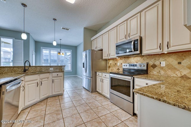 kitchen with light tile patterned floors, stainless steel appliances, decorative backsplash, decorative light fixtures, and a textured ceiling