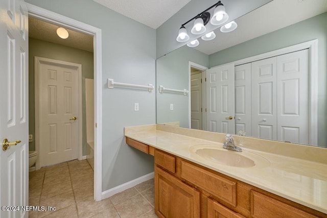 bathroom with a textured ceiling, tile patterned flooring, vanity, a tub to relax in, and toilet