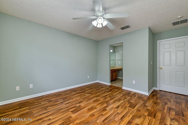 unfurnished bedroom featuring ceiling fan, connected bathroom, dark hardwood / wood-style flooring, and a textured ceiling