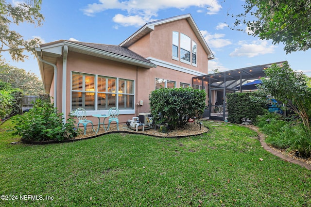 back of property with a lanai, central air condition unit, and a lawn