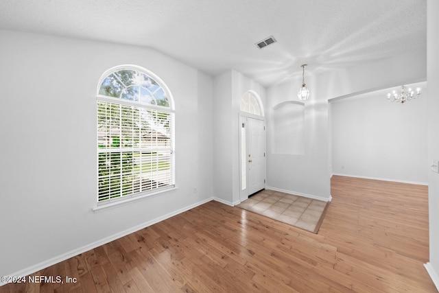 entryway with lofted ceiling, a chandelier, a textured ceiling, and light wood-type flooring