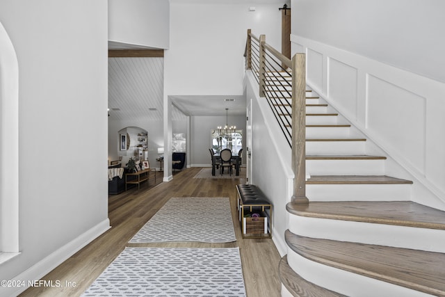 staircase featuring wood-type flooring, an inviting chandelier, and a high ceiling