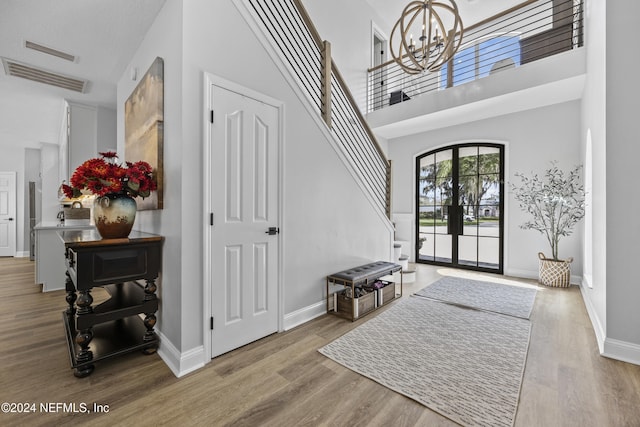 foyer entrance with a high ceiling, light hardwood / wood-style floors, french doors, and a notable chandelier