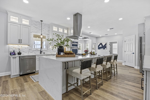 kitchen featuring island exhaust hood, appliances with stainless steel finishes, a kitchen island, white cabinetry, and hanging light fixtures