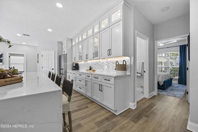 kitchen featuring a kitchen breakfast bar, light stone countertops, tasteful backsplash, dark hardwood / wood-style flooring, and white cabinetry