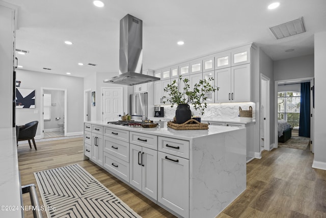 kitchen with a kitchen island, appliances with stainless steel finishes, island range hood, light stone counters, and white cabinetry