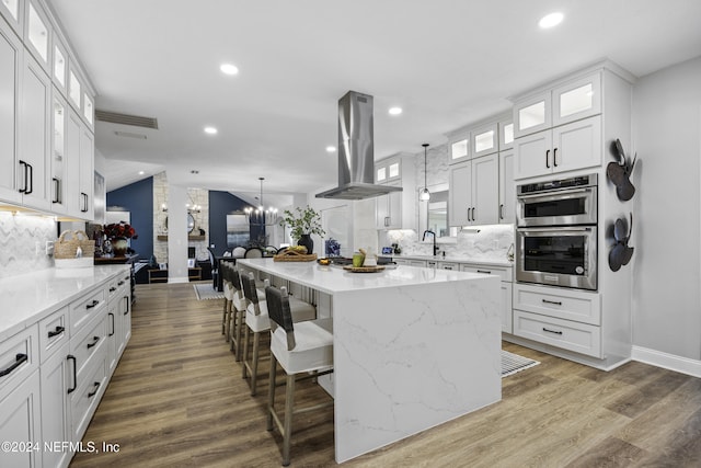 kitchen featuring a center island, tasteful backsplash, island range hood, white cabinets, and hardwood / wood-style flooring