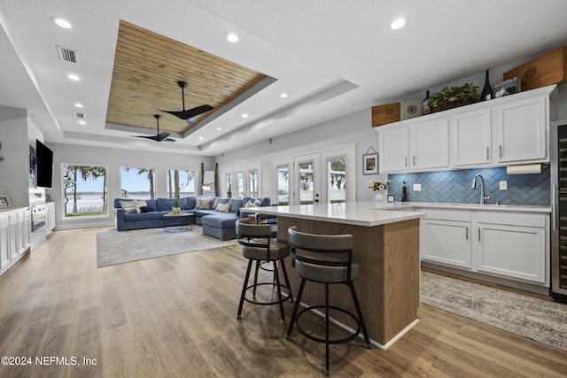 kitchen with a tray ceiling, ceiling fan, white cabinets, and light hardwood / wood-style floors