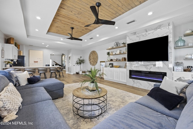 living room featuring ceiling fan, a raised ceiling, light wood-type flooring, and a premium fireplace