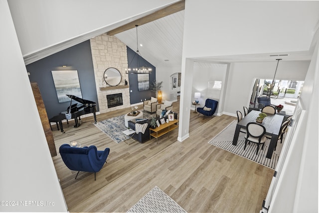 living room featuring high vaulted ceiling, a stone fireplace, beamed ceiling, wood-type flooring, and a chandelier