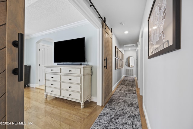 hall with a textured ceiling, light wood-type flooring, a barn door, and crown molding