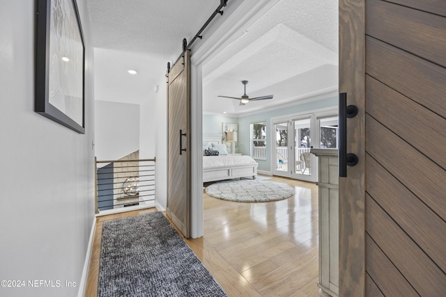 hallway featuring a barn door, a textured ceiling, and light hardwood / wood-style flooring