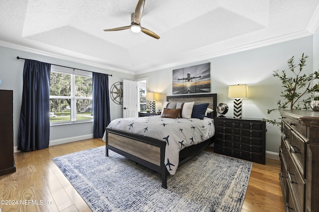 bedroom with light wood-type flooring, a raised ceiling, ceiling fan, and ornamental molding