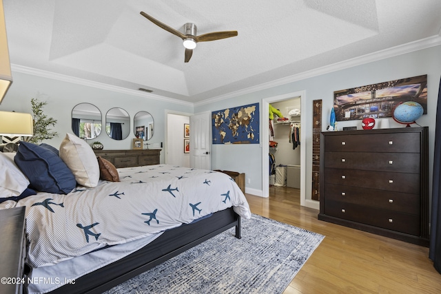 bedroom with ceiling fan, a raised ceiling, and a walk in closet