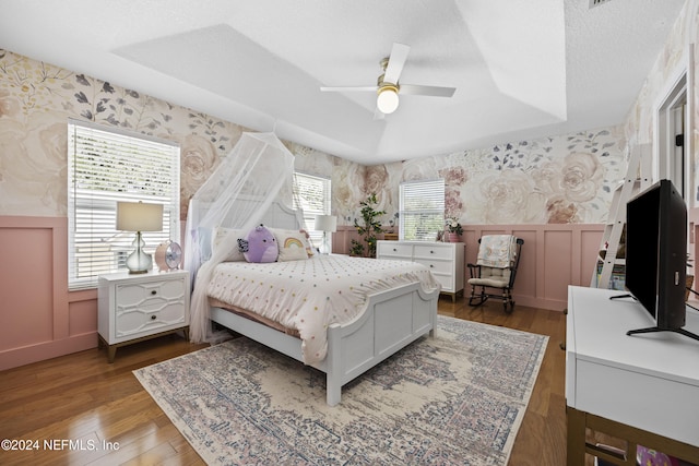 bedroom featuring a tray ceiling, multiple windows, ceiling fan, and dark hardwood / wood-style flooring