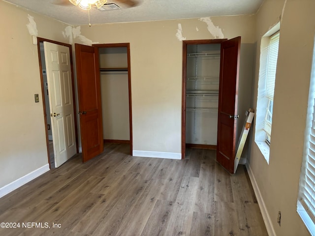 unfurnished bedroom with two closets, ceiling fan, a textured ceiling, and hardwood / wood-style flooring