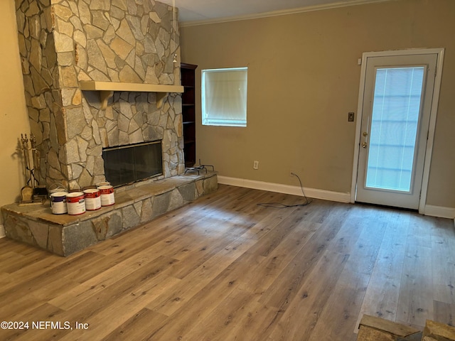 unfurnished living room featuring a stone fireplace, crown molding, and wood-type flooring