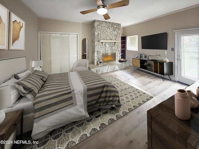 bedroom featuring ornamental molding, ceiling fan, hardwood / wood-style floors, a stone fireplace, and a closet