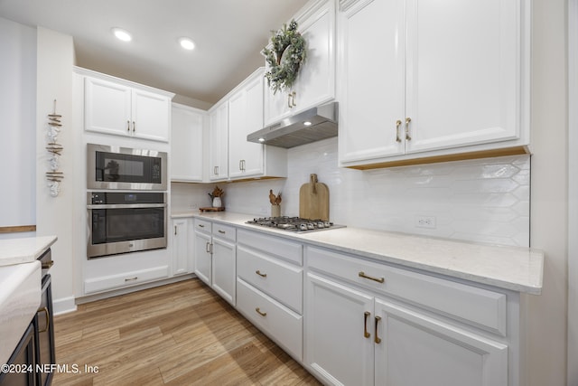 kitchen with white cabinets, light hardwood / wood-style flooring, decorative backsplash, light stone countertops, and stainless steel appliances