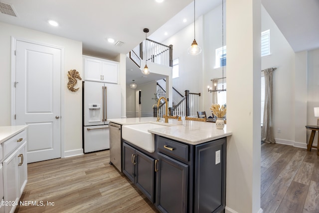 kitchen with light wood-type flooring, white cabinetry, hanging light fixtures, and a healthy amount of sunlight