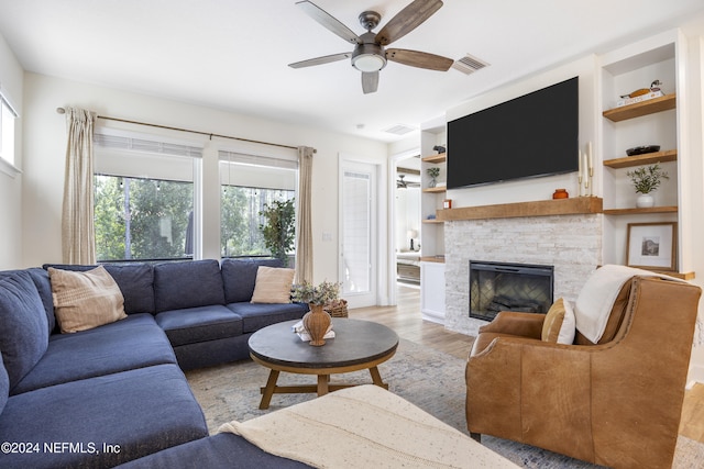 living room featuring a fireplace, light hardwood / wood-style floors, built in features, and ceiling fan