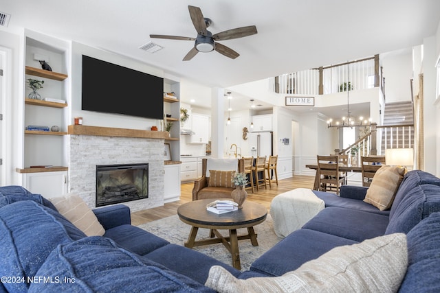 living room featuring sink, a stone fireplace, built in features, light hardwood / wood-style flooring, and ceiling fan with notable chandelier