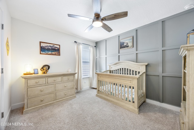 bedroom with a crib, light carpet, and ceiling fan