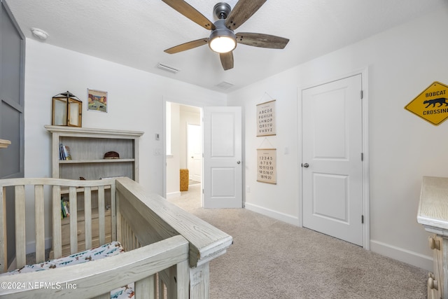 bedroom featuring a crib, light carpet, a textured ceiling, and ceiling fan