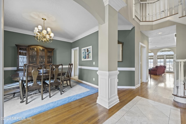 dining room with light wood-type flooring, an inviting chandelier, ornate columns, and ornamental molding