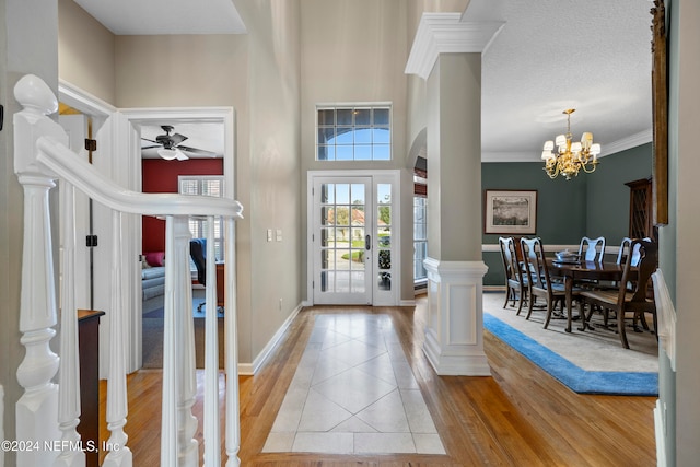 foyer entrance featuring ceiling fan with notable chandelier, a textured ceiling, light wood-type flooring, and crown molding