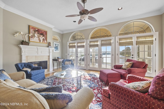 living room featuring a tile fireplace, ceiling fan, french doors, crown molding, and hardwood / wood-style flooring